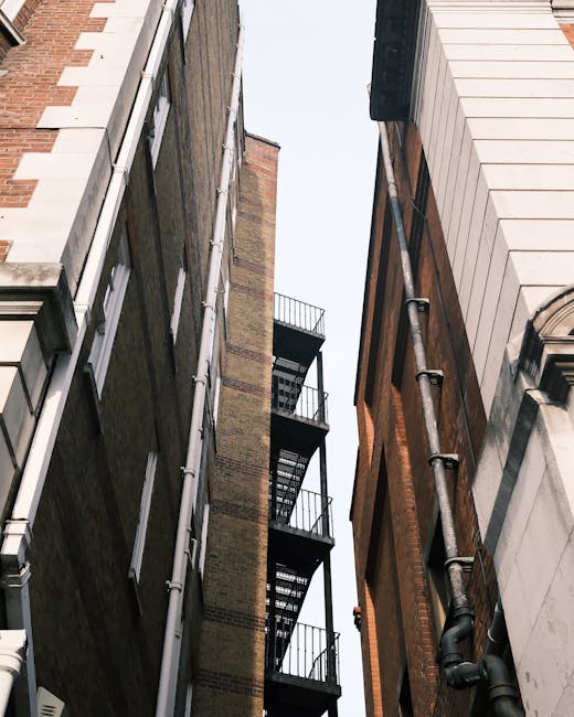 A cityscape view on Shoreditch High Street E1 featuring a variety of buildings with different architectural styles. In the foreground, there is a traditional brick building with multi-pane windows on